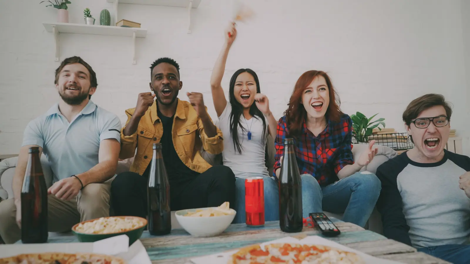 Friends cheering while watching a game on TV at an indoor party