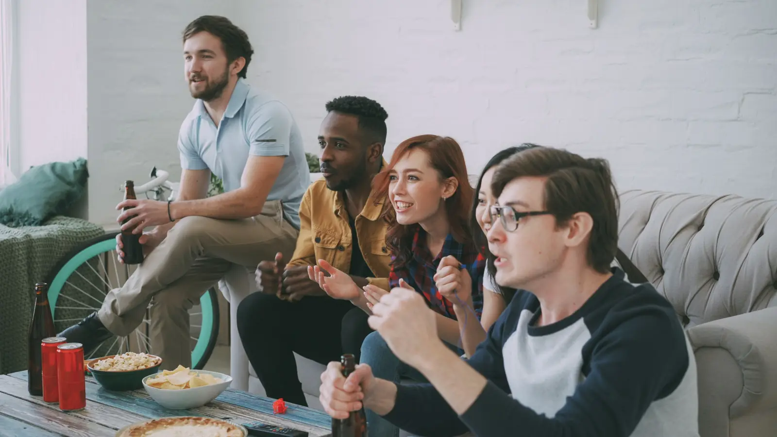 Group of friends watching a sports game on TV with snacks and drinks